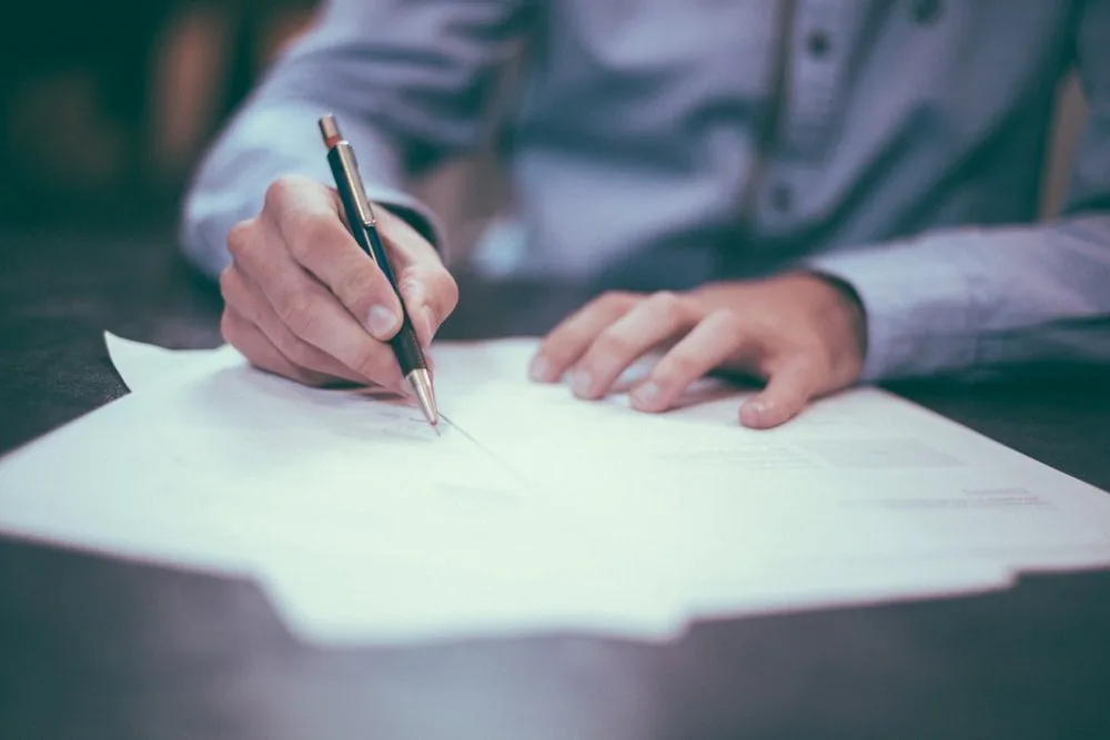 A hand signing a document with a pen