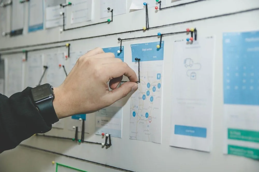 A hand arranging notes and diagrams on a wall